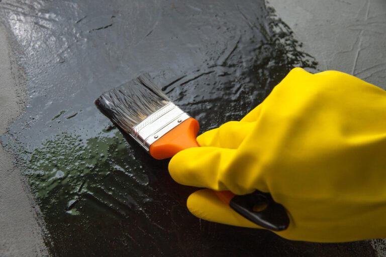 Mão usando pincel com luva amarela aplicando tinta preta em superfície